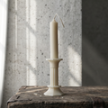 White candle in a decorative holder on a wooden surface with a textured wall background