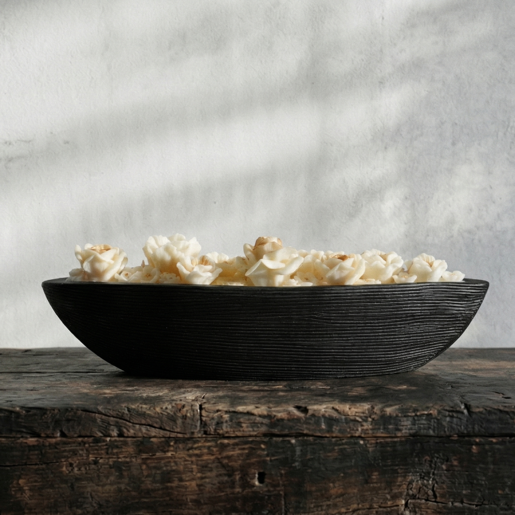 Black bowl filled with popcorn on a wooden surface with a gray textured background