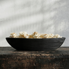 Black bowl filled with popcorn on a wooden surface with a gray textured background