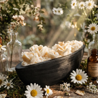 Black woven basket with white flowers on a wooden surface surrounded by daisies and bottles.