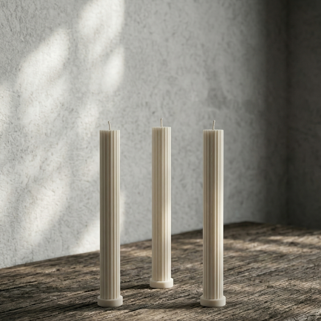 Three tall, thin candles on a wooden surface with a textured wall background