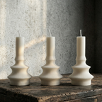 Three white candle holders on a wooden surface with a textured wall background