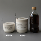 Two containers labeled 'Tropical Opulence Danang' with measurements and weights, next to a bottle on a gray background.